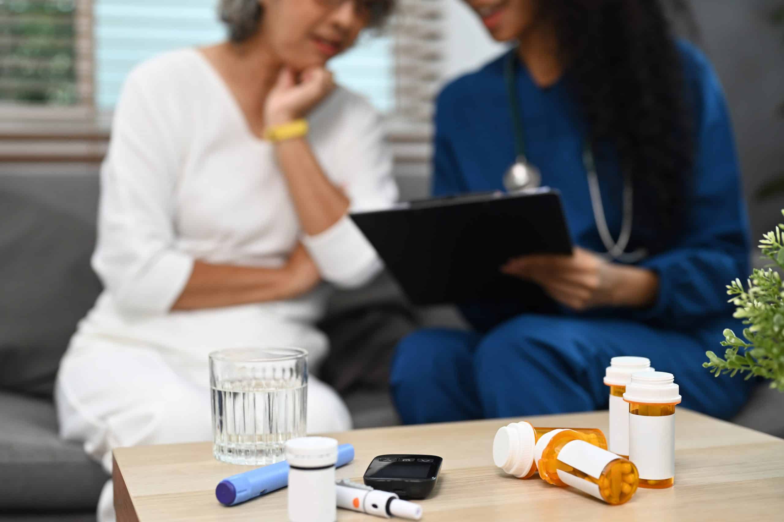 Pill bottles on table with healthcare worker and senior woman sitting on background.